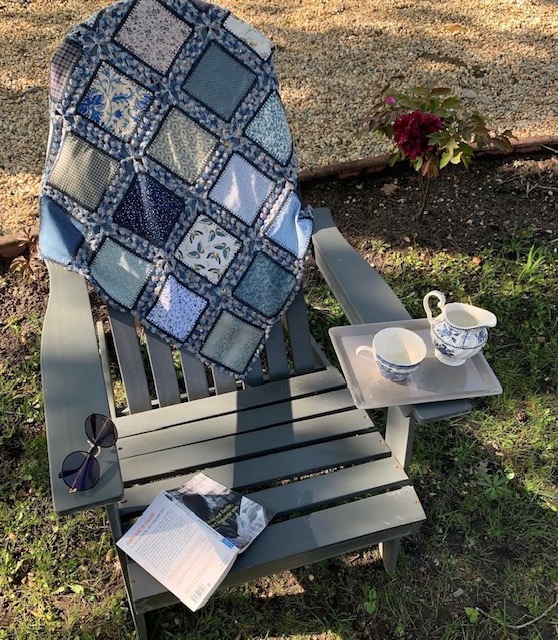 Plaid patchwork posé sur une chaise en extérieur avec tasse de thé, projet textile terminé